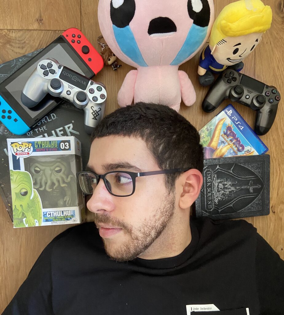 Anthony L. Wolf, Writer & Narrative Designer, lies upon a multitude of items, from an Isaac plush to a couple of PS4 controllers, disposed in a semi-circle around his head.